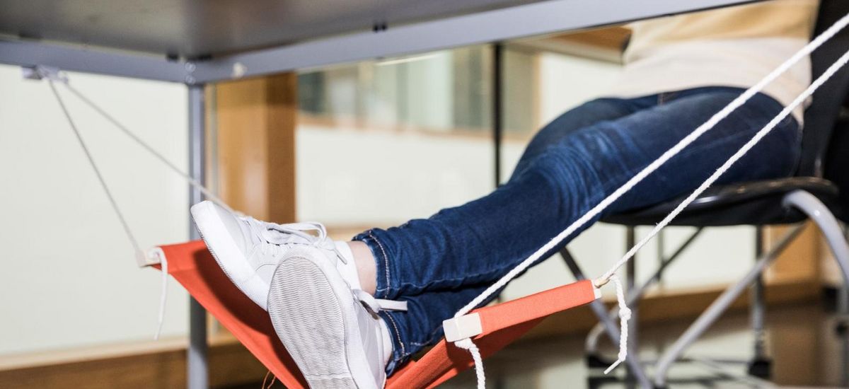 Feet are seen in a small hammock under a desk.