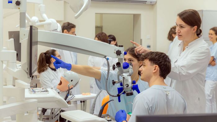 Zu sehen sind Zahnmedizin-Studierende, die an einer Puppe auf einem Behandlungsstuhl eine Zahnbehandlung üben.