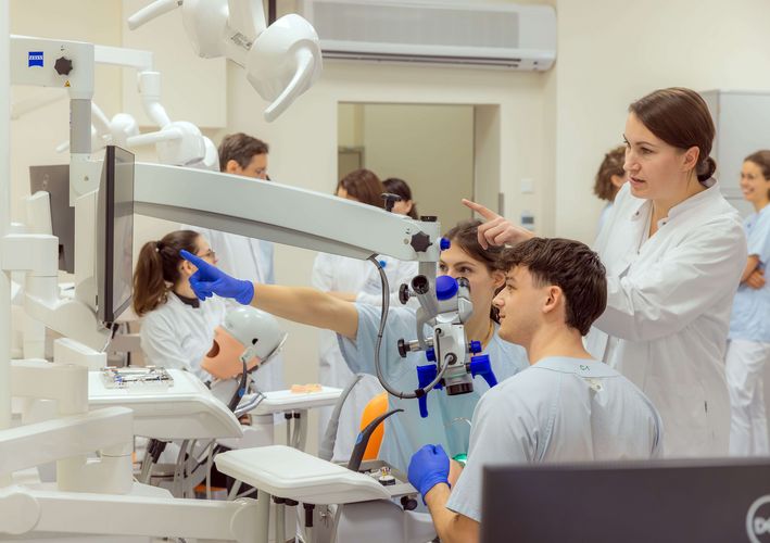 Zu sehen sind Zahnmedizin-Studierende, die an einer Puppe auf einem Behandlungsstuhl eine Zahnbehandlung üben.