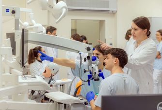 Zu sehen sind Zahnmedizin-Studierende, die an einer Puppe auf einem Behandlungsstuhl eine Zahnbehandlung üben.