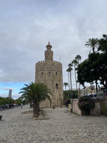 Der Torre del Oro bei Tageslicht von der Seite fotografiert. Drumherum sind Palmen und Straßen zu sehen.