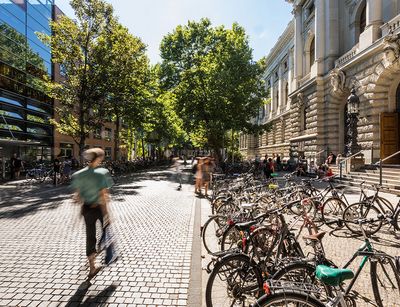 Studierende vor der Universitätsbibliothek. Ihre Umrisse sind unscharf, da sie in Bewegung sind