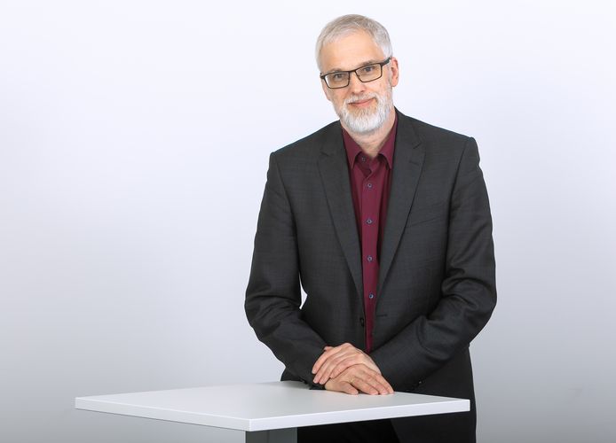 Ein Mann mit dunklem Anzug und rotem Hemd, grauem Vollbart und Brille steht an einem Tisch und schaut in die Kamera. Professor Dr. Gert Pickel, Foto: Universität Leipzig.
