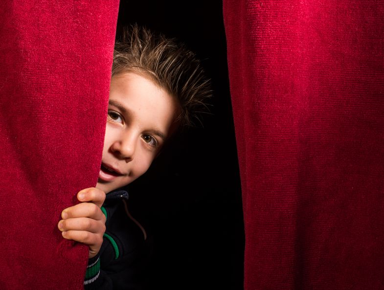 Zu sehen ist ein Kind, das hinter einem Vorhang hervorschaut.