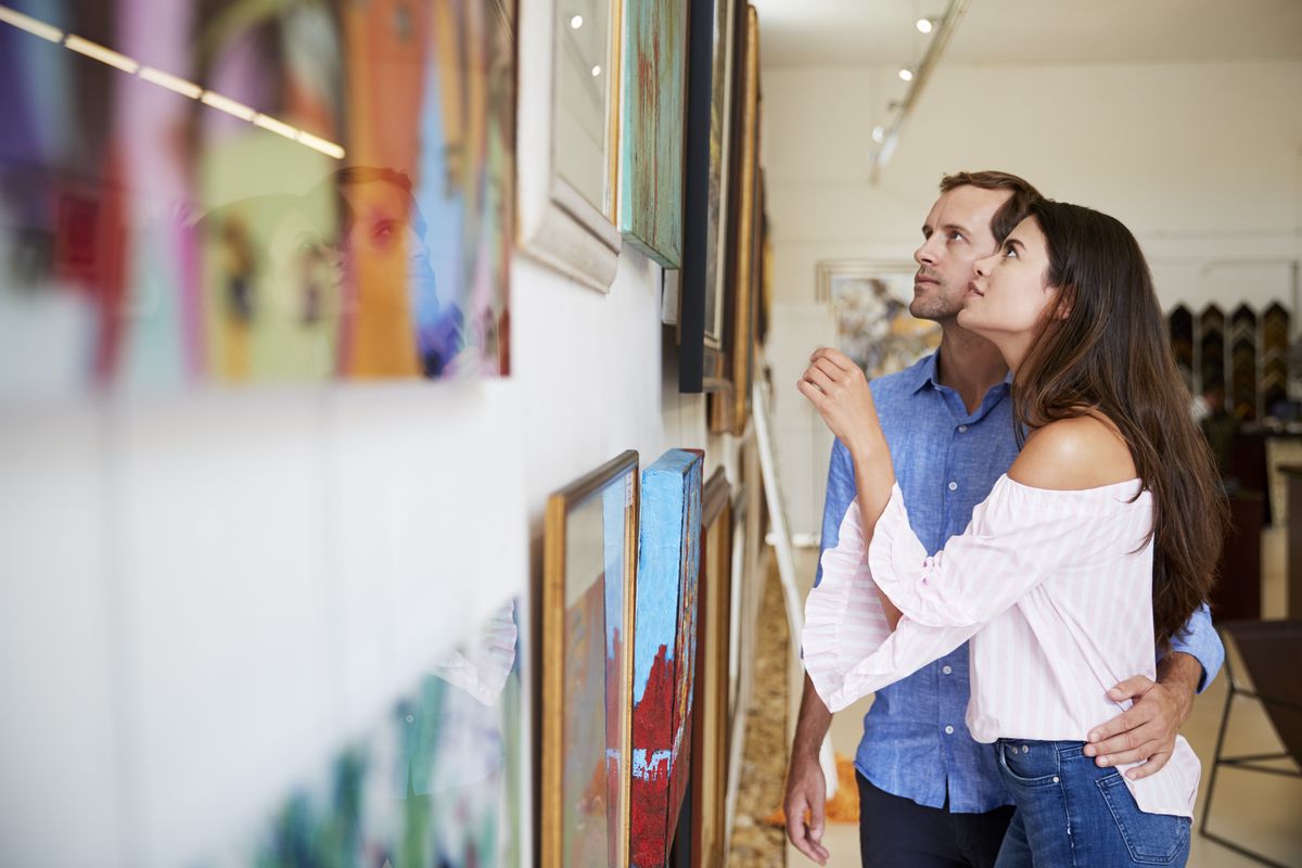 Zu sehen ist ein junges Paar, das sich in einer Galerie gemeinsam Bilder ansieht.