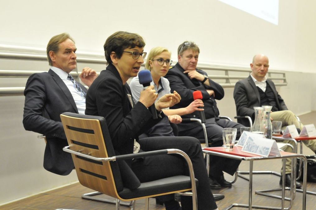 zur Vergrößerungsansicht des Bildes: Fünf Personen sitzen in einem Halbkreis auf einem Podium. Die Dame im Vordergrund hält ein Mikrofon und spricht in Richtung des Publikums des Donnerstagsdiskurses.