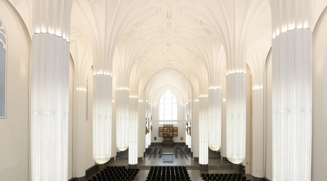 Blick von Orgelempore im Paulinum in Richtung Altar; zu sehen sind die Epitaphie an den Wänden, die beleuchteten Glassäulen, der Altar und die Stuhlreihen im Innenraum