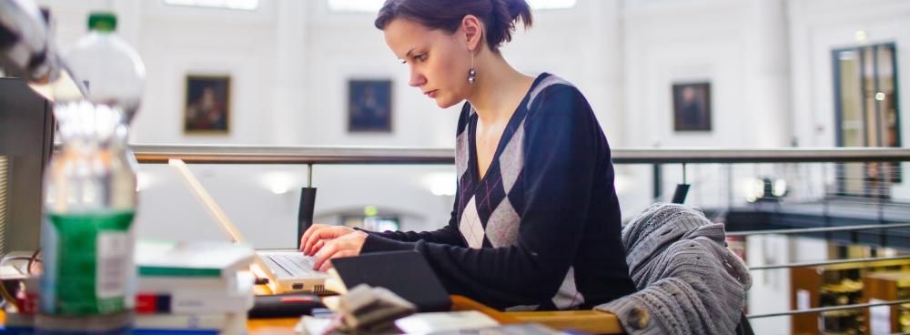 Foto: Eine Studentin sitzt an einem Arbeitsplatz in der Bibliotheca Albertina und tippt etwas in den Laptop