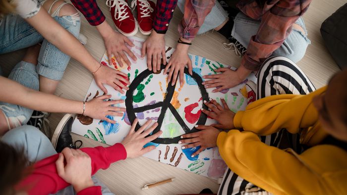 Junge Menschen sitzen im Kreis und halten ihre Hände über eine Unterlage mit farbigen Handabdrücken und einem Peace-Zeichen.