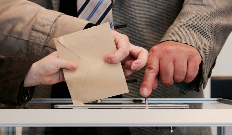 Zwei Hände werfen einen Briefumschlag in eine Wahlurne