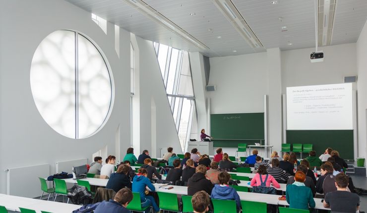 Foto: Studierende während einer Vorlesung in einem Hörssal mit grünen Stühlen