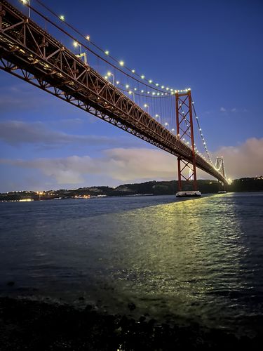 beleuchtete Brücke bei Nacht vom anderen Tejo Ufer von schräg unten fotografiert
