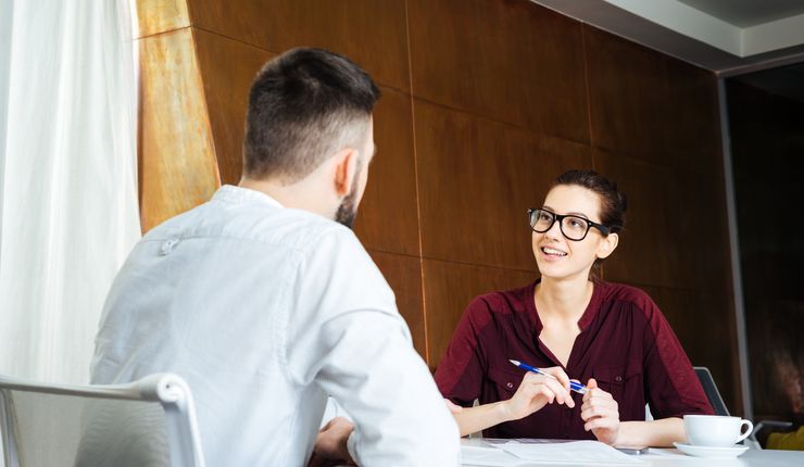 Two people sit at a table in a professional environment and are in conversation