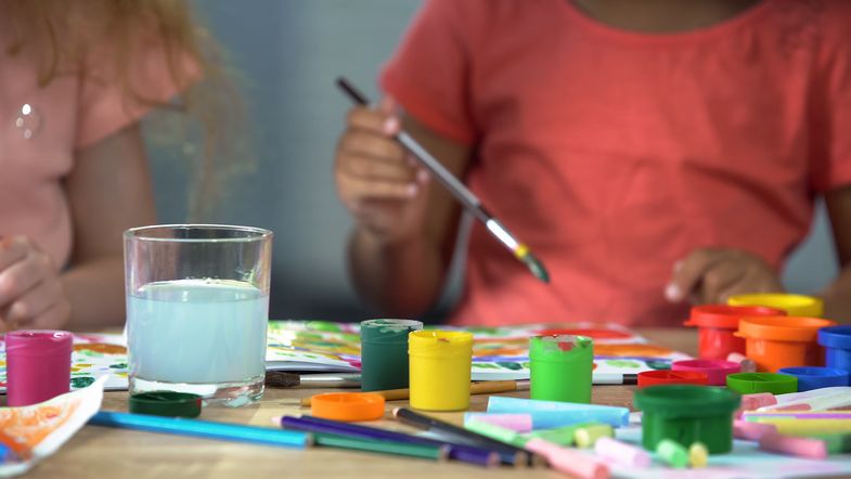 Zu sehen sind zwei Kinder an einem Tisch mit Malutensilien.