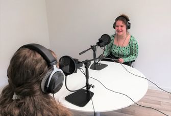Zwei Studentinnen mit Mikrofonen und Kopfhörern nehmen einen Podcast auf. 