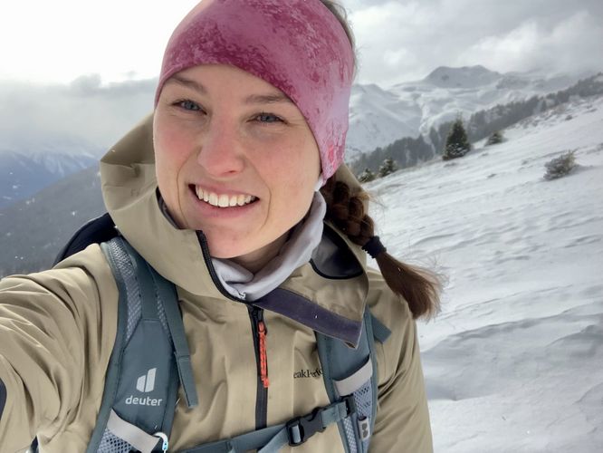 Farbfoto: Vor einer schneebedeckten Berglandschaft lächelt eine Frau in die Kamera