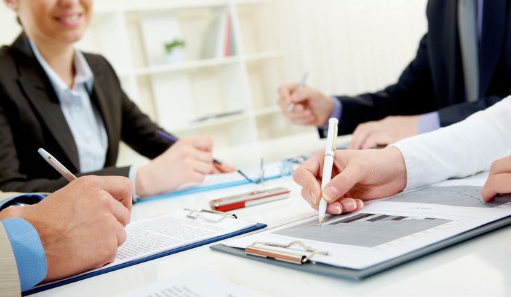 Menschen sitzen mit Papier und Stift an einem Tisch und beraten sich