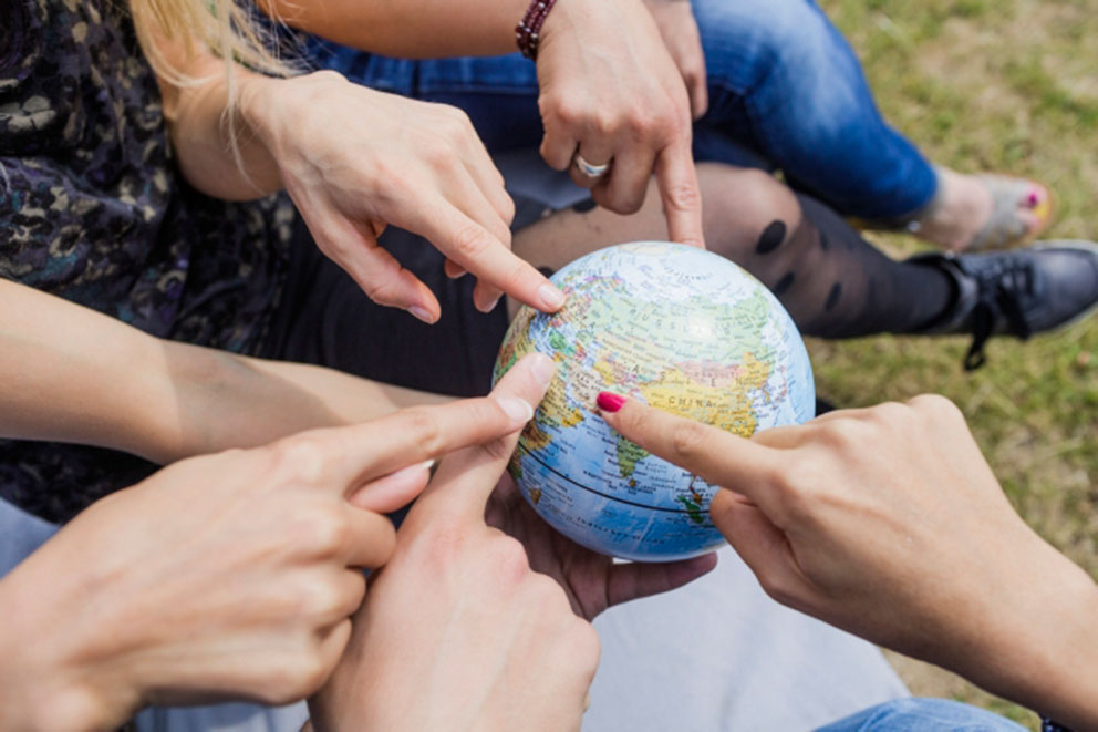 Studierende der Universität Leipzig halten einen Globus in den Händen und zeigen sich gegenseitig ihre Herkunftsländer.