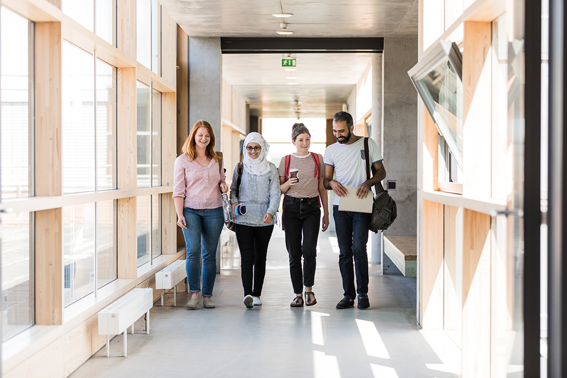 Vier Studierende laufen einen Gang im Geisteswissenschaftlichen Zentrum entlang und beschreiten damit den Leipziger Weg in Lehre und Forschung.