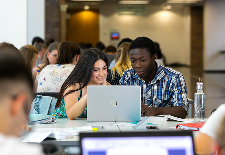 Studierende der Universität Leipzig sitzen zusammen an einer Arbeitsinsel und blicken auf einen Laptop-Bildschirm.