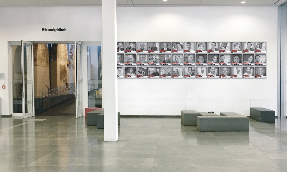 Frontalansicht Innenbereich Neues Augusteum mit Blick auf den Übergang zum Hörsaalgebäude, rechts davon sind ca. 40 quadratische Portraitaufnahmen von Alumni der Universität Leipzig an die Wand angebracht. Die Aufnahme ist eine Computeranimation und kein realistisches Foto. 